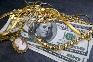 Broken gold jewelry pieces and scrap gold items on top of several $100 bills