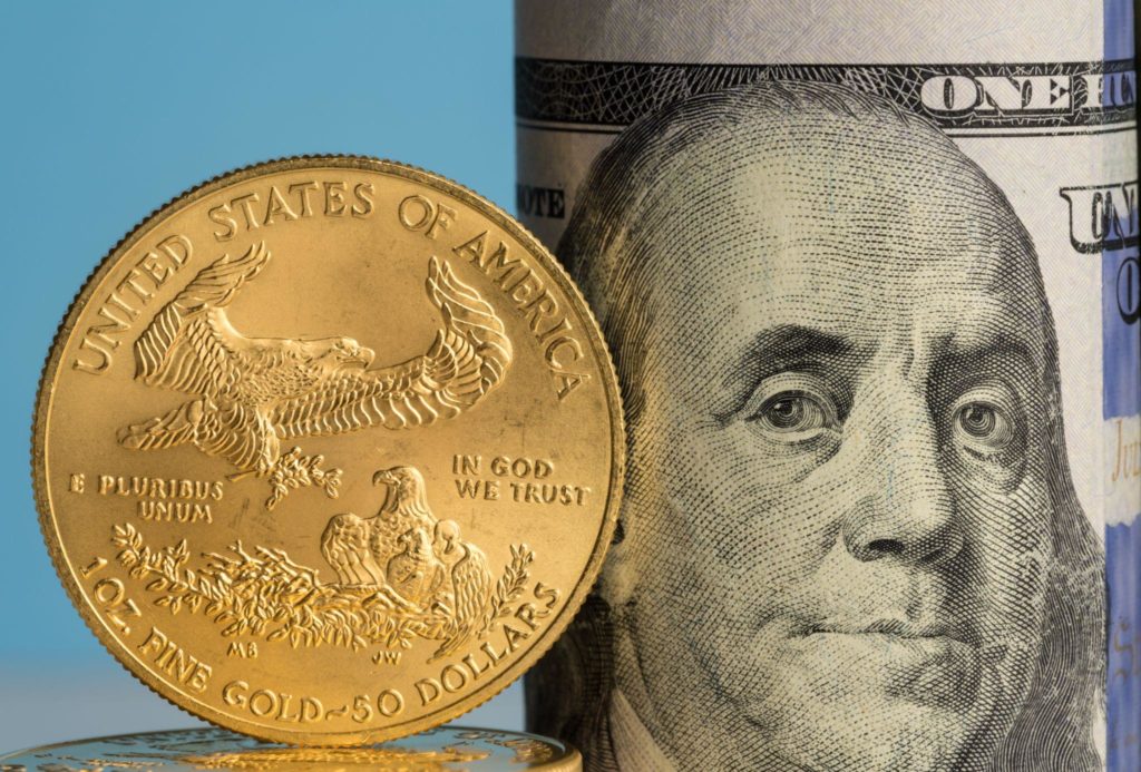 Pure gold eagle coin in front of Benjamin Franklin face on rolled bankrolls of USA dollar bills