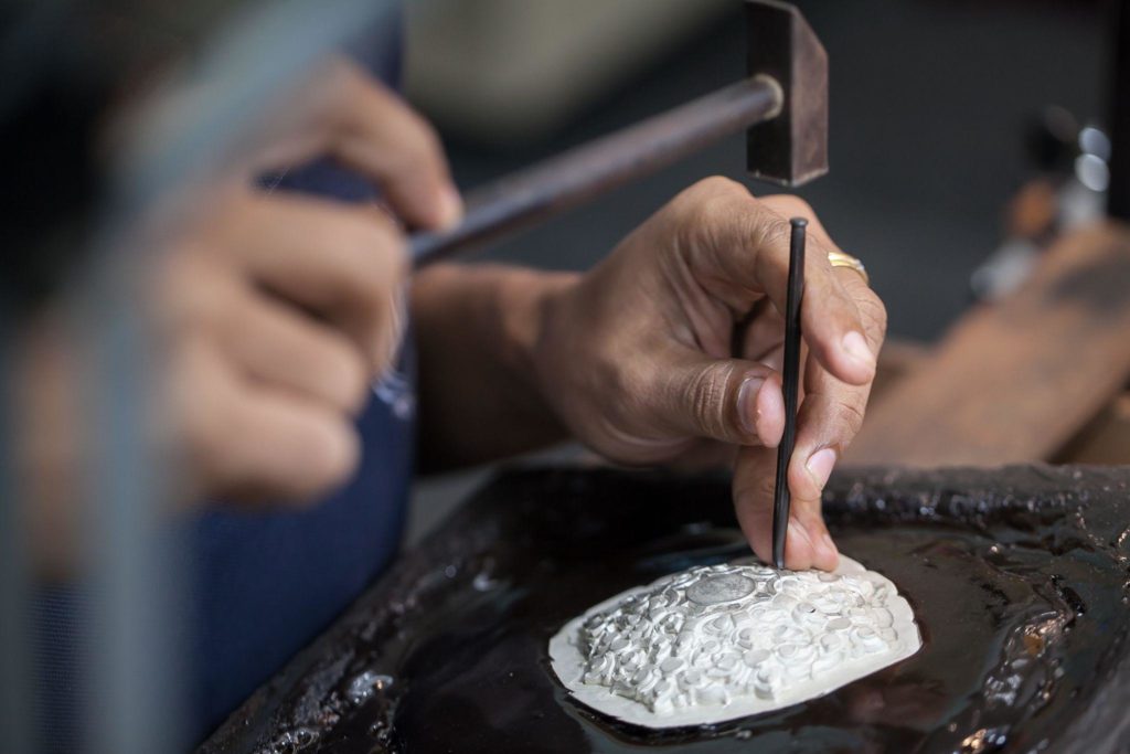 silversmith using hammer on silver plate