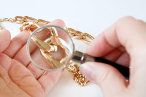 gold chain jewelry inspected by hand with magnifying glass