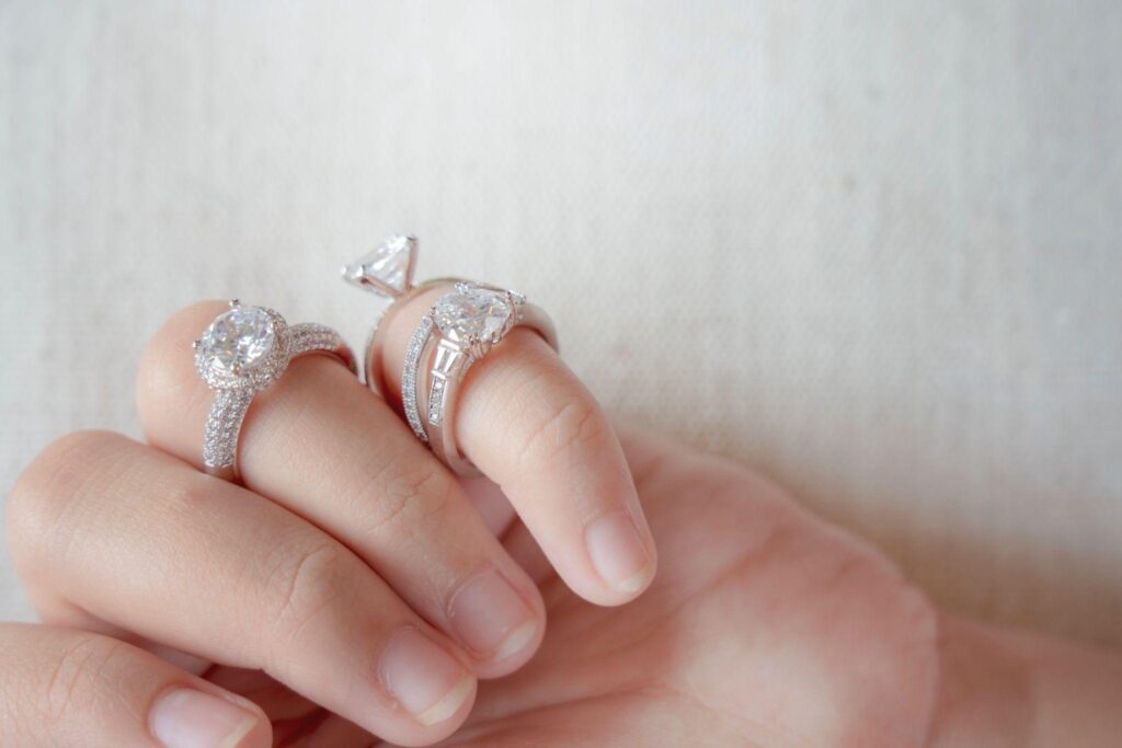 Four white gold and silver rings on fingers. 